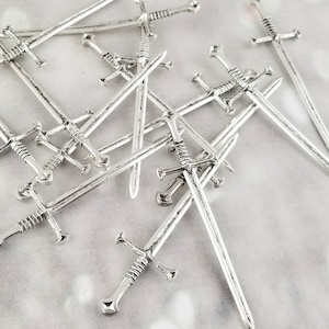 Könnte beinhalten: Eine Gruppe silberfarbener Cocktailstecker in Schwertform. Die Stecker sind in einem zufälligen Muster angeordnet, wobei sich einige überlappen.