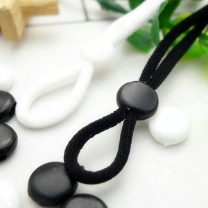 May include: Black and white elastic cord with black plastic stoppers. The cord is looped and tied together with a knot. The stoppers are round and have a hole in the center.
