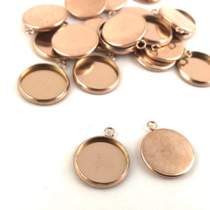 May include: A group of rose gold metal round pendant trays with a loop for hanging. The trays are empty and ready to be filled with resin, epoxy, or other materials.