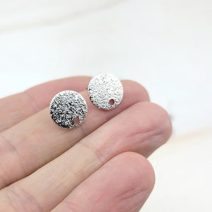 May include: Two silver-toned round metal earring blanks with a textured surface and a small hole in the center.