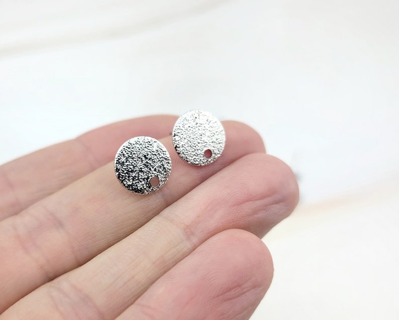 May include: Two silver-toned round metal earring blanks with a textured surface and a small hole in the center.