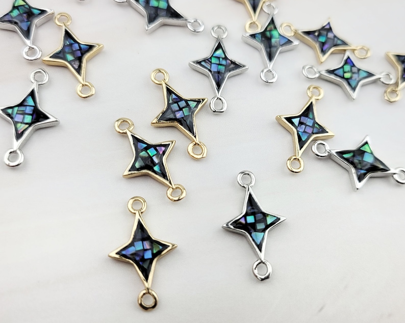 May include: A group of 15 gold and silver star-shaped charms with a blue and green abalone shell inlay. The charms have two jump rings for attaching to jewelry.