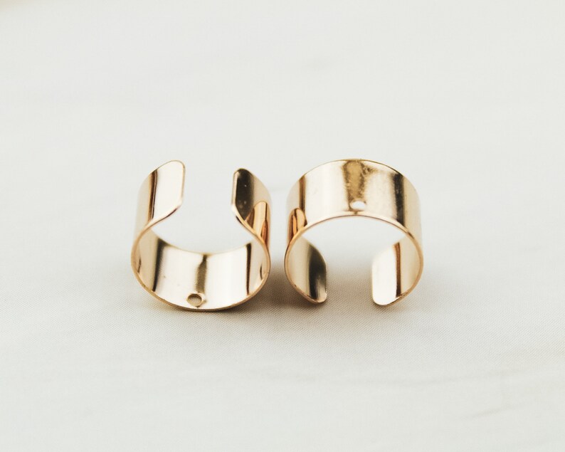 May include: Two gold-toned metal ear cuffs. Each cuff is a simple, rounded band with a small hole in the center.