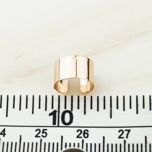 May include: A gold-toned metal ring with a small hole in the center. The ring is about 1 inch in diameter and is shown on a white surface with a ruler.