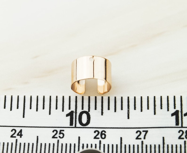 May include: A gold-toned metal ring with a small hole in the center. The ring is about 1 inch in diameter and is shown on a white surface with a ruler.