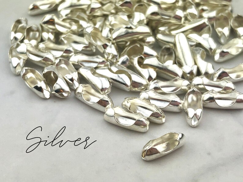 Puede incluir: Un conjunto de cierres de joyer&iacute;a plateados brillantes. Los cierres tienen forma ovalada con un dise&ntilde;o curvo y una peque&ntilde;a abertura en cada extremo. La palabra "Silver" est&aacute; escrita en cursiva en la parte inferior izquierda.