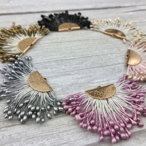 May include: Six decorative fan-shaped embellishments with a gold metal accent. The embellishments are in various colors, including black, white, gold, silver, and pink.