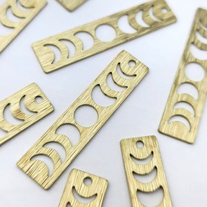 May include: A set of eight gold-colored metal charms featuring a crescent moon design. Each charm is rectangular and has a different phase of the moon cut out. The charms are perfect for adding a touch of whimsy to jewelry or crafts.