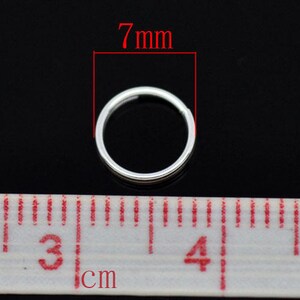 May include: A silver jump ring measuring 7mm in diameter. The ring is shown next to a ruler with centimeter markings.