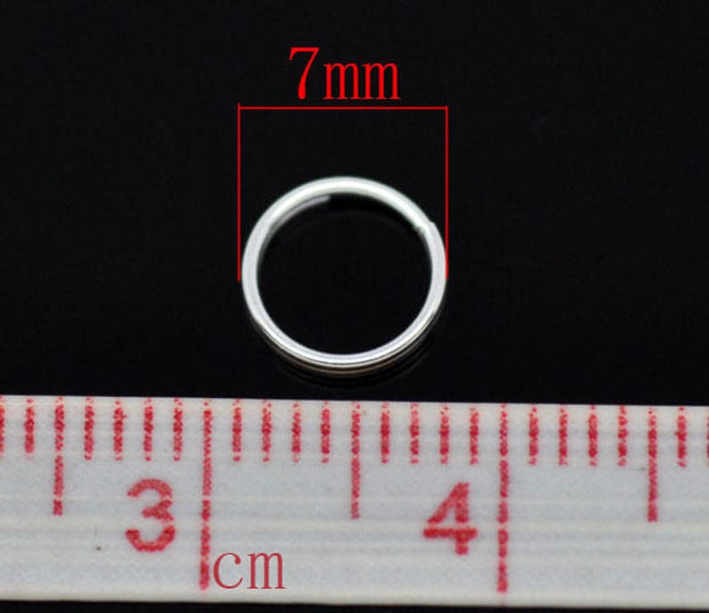 May include: A silver jump ring measuring 7mm in diameter. The ring is shown next to a ruler with centimeter markings.
