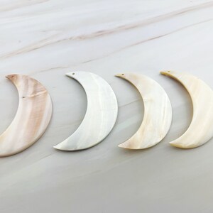 May include: Four white and beige crescent moon shaped pendants with a hole at the top for hanging.