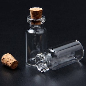 Könnte beinhalten: Zwei klare Glasflaschen mit Korkstopfen. Die Flaschen sind klein und zylindrisch. Die Korkstopfen sind braun und haben eine natürliche Textur.