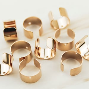 May include: Ten gold-toned metal rings with a small hole in each. The rings are open on one side and have a rounded shape.