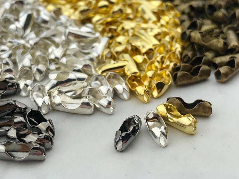 Puede incluir: Un surtido de cierres de joyer&iacute;a met&aacute;licos en varios acabados: plata, oro y bronce. Los cierres son peque&ntilde;os, curvos y dise&ntilde;ados para conectar piezas de joyer&iacute;a. La imagen muestra una vista de cerca de los cierres, destacando su forma y brillo met&aacute;lico.