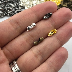 Puede incluir: Primer plano de varios conectores de cadena de bolas met&aacute;licos en varios acabados: plata, negro, oro y lat&oacute;n antiguo. Estos peque&ntilde;os componentes curvos se utilizan para conectar cadenas de bolas para la fabricaci&oacute;n de joyas y otros proyectos de artesan&iacute;a.