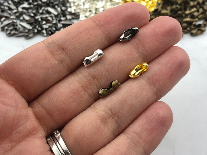Puede incluir: Primer plano de varios conectores de cadena de bolas met&aacute;licos en varios acabados: plata, negro, oro y lat&oacute;n antiguo. Estos peque&ntilde;os componentes curvos se utilizan para conectar cadenas de bolas para la fabricaci&oacute;n de joyas y otros proyectos de artesan&iacute;a.