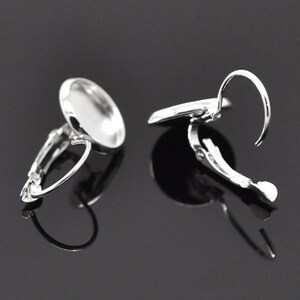 May include: A pair of silver clip-on earring settings with round bezels. The bezels are designed to hold a cabochon or other flat-backed embellishment.