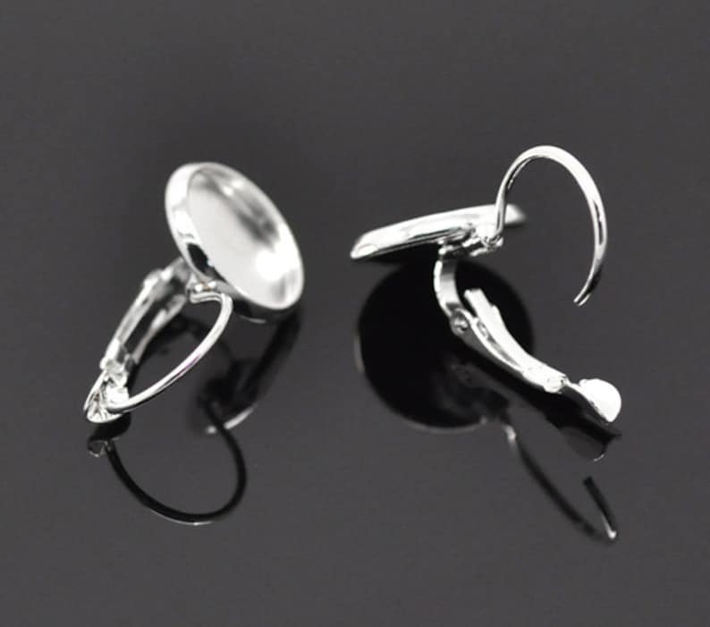 May include: A pair of silver clip-on earring settings with round bezels. The bezels are designed to hold a cabochon or other flat-backed embellishment.