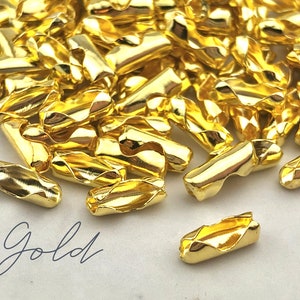 Puede incluir: Un conjunto de cierres de joyer&iacute;a dorados y brillantes. Los cierres son peque&ntilde;os, cil&iacute;ndricos y tienen un dise&ntilde;o curvo &uacute;nico. La palabra "Gold" est&aacute; escrita en cursiva en la esquina inferior izquierda. Estos cierres probablemente se utilizan para collares o pulseras.