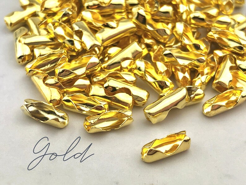 Puede incluir: Un conjunto de cierres de joyer&iacute;a dorados y brillantes. Los cierres son peque&ntilde;os, cil&iacute;ndricos y tienen un dise&ntilde;o curvo &uacute;nico. La palabra "Gold" est&aacute; escrita en cursiva en la esquina inferior izquierda. Estos cierres probablemente se utilizan para collares o pulseras.