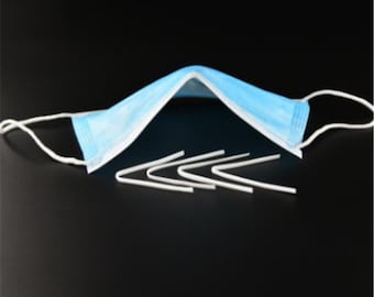 Puede incluir: Primer plano de una mascarilla facial azul claro con alambre nasal blanco. La mascarilla está doblada por la mitad y hay seis reemplazos de alambre nasal de plástico blanco delante de ella.