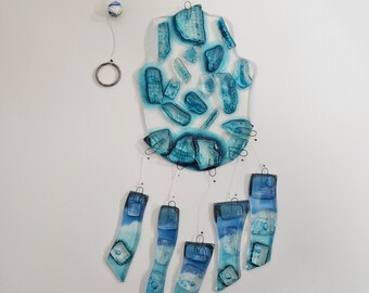 Könnte beinhalten: Ein handgefertigter Glas-Windspiel in Form einer Hamsa-Hand. Das Windspiel hat blaue und weiße Glasteile. Das Design umfasst eine klare Glas-Handform mit blauen Glasakzenten und hängenden blauen Glasteilen.