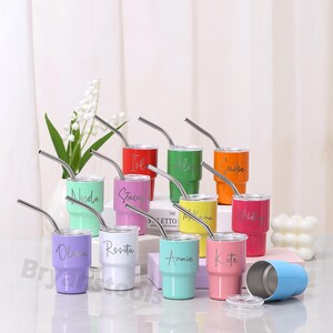 May include: A collection of personalized stainless steel tumblers in various colors, each with a name etched on the front. The tumblers have silver straws and clear lids. Colors include red, green, orange, pink, purple, white, yellow, and blue.