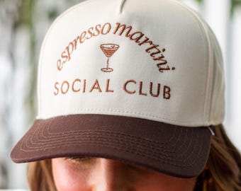 Puede incluir: Gorra de béisbol color crema con visera y botón superior marrón. La gorra presenta el texto bordado "espresso martini SOCIAL CLUB" en marrón, con un gráfico de copa de martini encima de "SOCIAL CLUB".