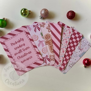 May include: A collection of pink and red Christmas-themed bookmarks with various patterns, including stripes, bows, gingerbread men, and a checkerboard design. One bookmark features the text "Probably reading small town Christmas romance."