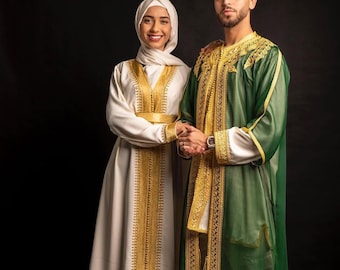 Può includere: Una coppia vestita con abiti tradizionali marocchini. La donna indossa un vestito bianco con ricami dorati e un velo bianco. L'uomo indossa una tunica verde con ricami dorati.