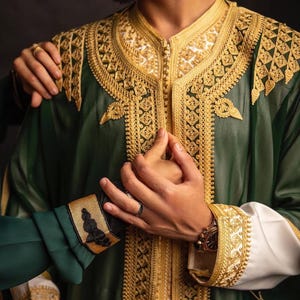 May include: Green and gold embroidered robe with white sleeves. The robe features intricate gold embroidery along the collar, cuffs, and front. The sleeves are white with gold detailing. The image shows a close-up of the robe.