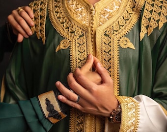 Può includere: Abito verde con ricami dorati e maniche bianche. L'abito presenta intricati ricami dorati sul colletto, sui polsini e sul davanti. Le maniche sono bianche con dettagli dorati. Primo piano dell'abito.