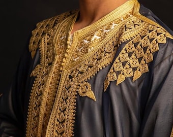 Può includere: Una veste grigio scuro con ricami dorati intricati intorno allo scollo e alle spalle. La veste ha maniche lunghe e una vestibilità ampia. Lo sfondo è nero.