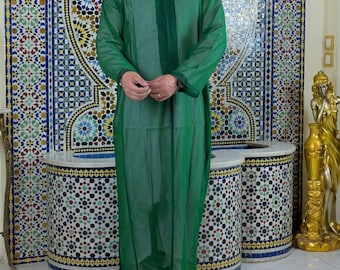 Può includere: Una lunga veste verde smeraldo con finiture verde scuro e colletto alla coreana. La veste è indossata con pantofole gialle. Lo sfondo presenta un muro a mosaico ed elementi decorativi.