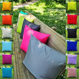 Könnte beinhalten: Eine Sammlung farbenfroher quadratischer Zierkissen in verschiedenen Farbtönen, darunter Gelb, Orange, Weiß, Blau, Pink und Grau. Die Kissen sind auf einer Holzbank und auf dem Rasen angeordnet und zeigen ihre lebendigen Farben und Texturen.
