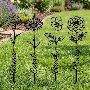 Puede incluir: Cuatro estacas de jardín de metal negro con siluetas florales. Cada estaca muestra un diseño de flor único con un nombre integrado en el tallo: Teresa, Coral, Brook y Mary. Las estacas están colocadas verticalmente en un césped verde.