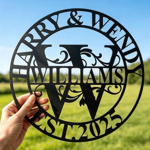 May include: A circular black metal sign featuring the names HARRY & WENDY arched along the top, the surname WILLIAMS centered across a large letter W, and the text EST. 2025 at the bottom, all connected by decorative scrollwork details.