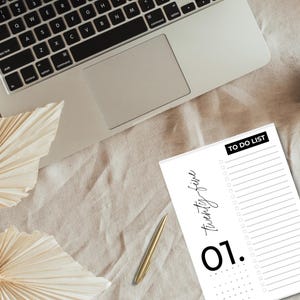 Puede incluir: Un bloc de notas blanco de lista de tareas con texto negro que dice "twenty-five" y "01." El bloc de notas tiene un encabezado negro que dice "TO DO LIST".