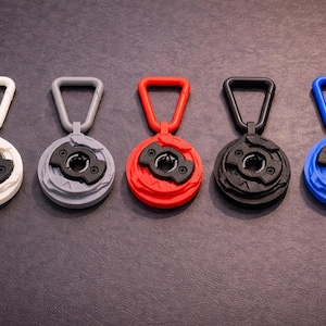 May include: Five circular objects in a row, each with a handle. The colours are white, grey, red, black, and blue. Each has a black centre with a unique design. The handles match the colour of the outer ring of each object.