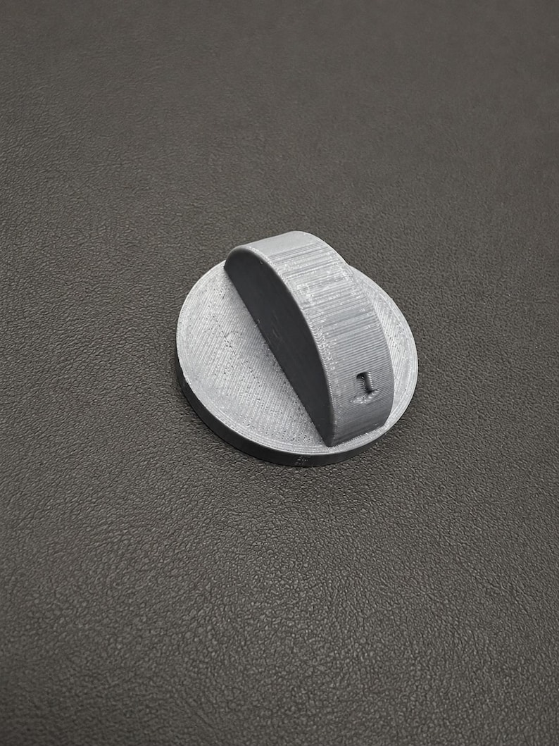 May include: A circular gray plastic control knob featuring a raised vertical ridge across the center. The side of the ridge displays the embossed number 1. The surface of the knob shows a textured finish consistent with 3D printed manufacturing.