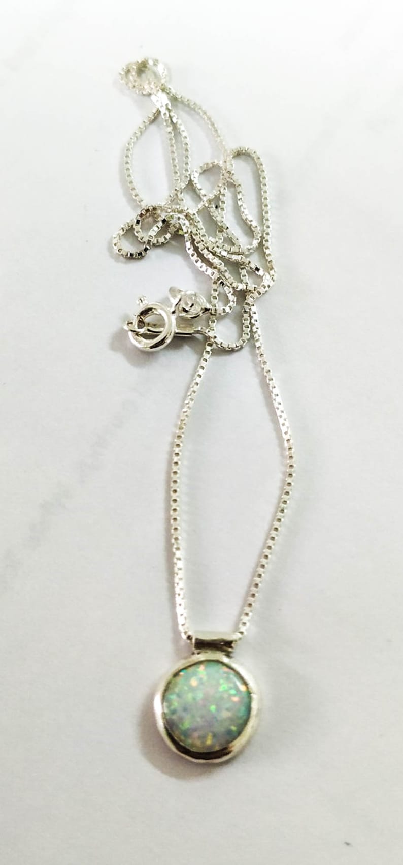 May include: A silver chain necklace with a round opal pendant. The opal is white with green and blue flashes.