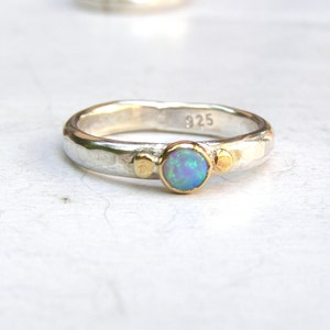 May include: A silver ring with a blue opal gemstone and gold accents. The ring is stamped with "925" on the inside.