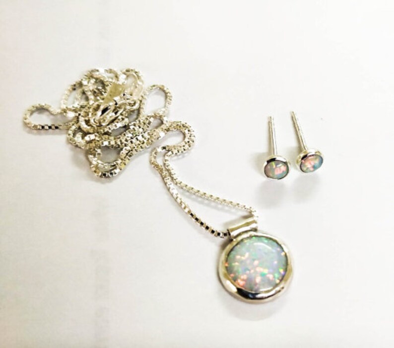 May include: A silver necklace with a round opal pendant and matching opal stud earrings. The necklace has a delicate chain.