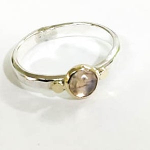 May include: A silver ring with a light pink oval gemstone and two gold accents.