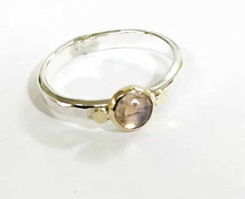 May include: A silver ring with a light pink oval gemstone and two gold accents.