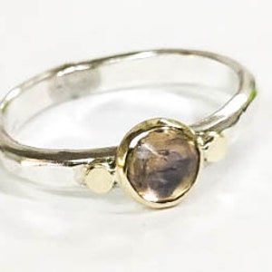 May include: A silver ring with a hammered finish and a round, brown gemstone set in a gold bezel. The ring has two smaller gold accents on either side of the gemstone.