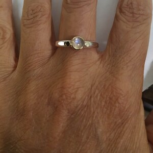 May include: A silver ring with a round, iridescent moonstone set in the center.