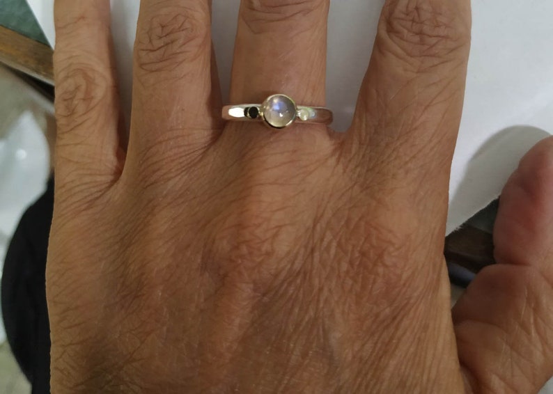 May include: A silver ring with a round, iridescent moonstone set in the center.