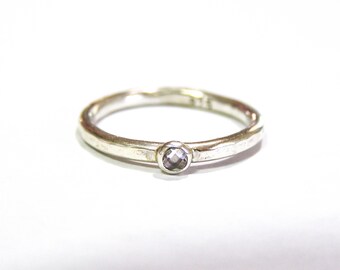 May include: A silver ring with a small, clear gemstone set in the center.