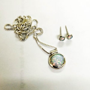 May include: A silver necklace with a round opal pendant and matching opal earrings. The opal is a milky white color with flashes of green and blue.